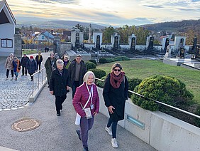 Eine Gruppe an Menschen spaziert durch den Friedhof